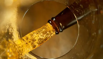 Cerveja a ser vertida de uma garrafa para um copo vista pelo interior do copo