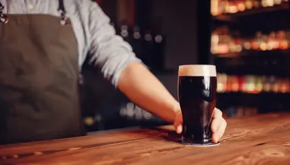 A person pouring a glass of dark beer at a bar counter.