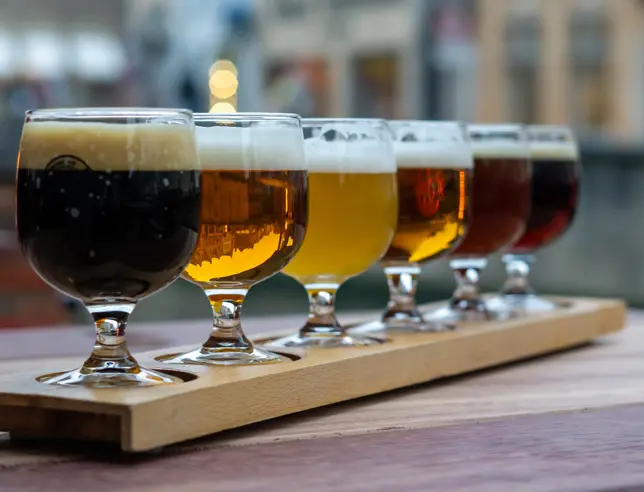 A set of beer glasses in different colors on a wooden board.