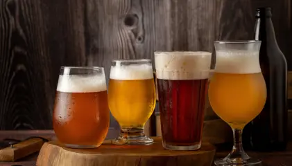 Four glasses of beer in different colors, with foam, on a wooden table.