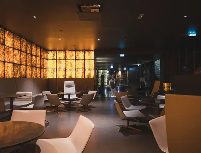 Interior of a modern tasting space with light-coloured tables and chairs, warm lighting and illuminated decorative walls.