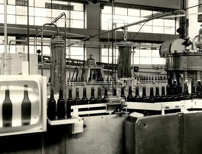 Vintage industrial bottle filling line with multiple bottles aligned inside a beer factory.