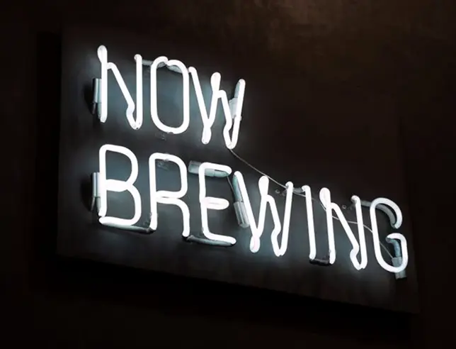 Letreiro luminoso com a frase “Now Brewing”.