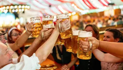 Grupo de pessoas a brindar com canecas de cerveja num festival tradicional alemão.